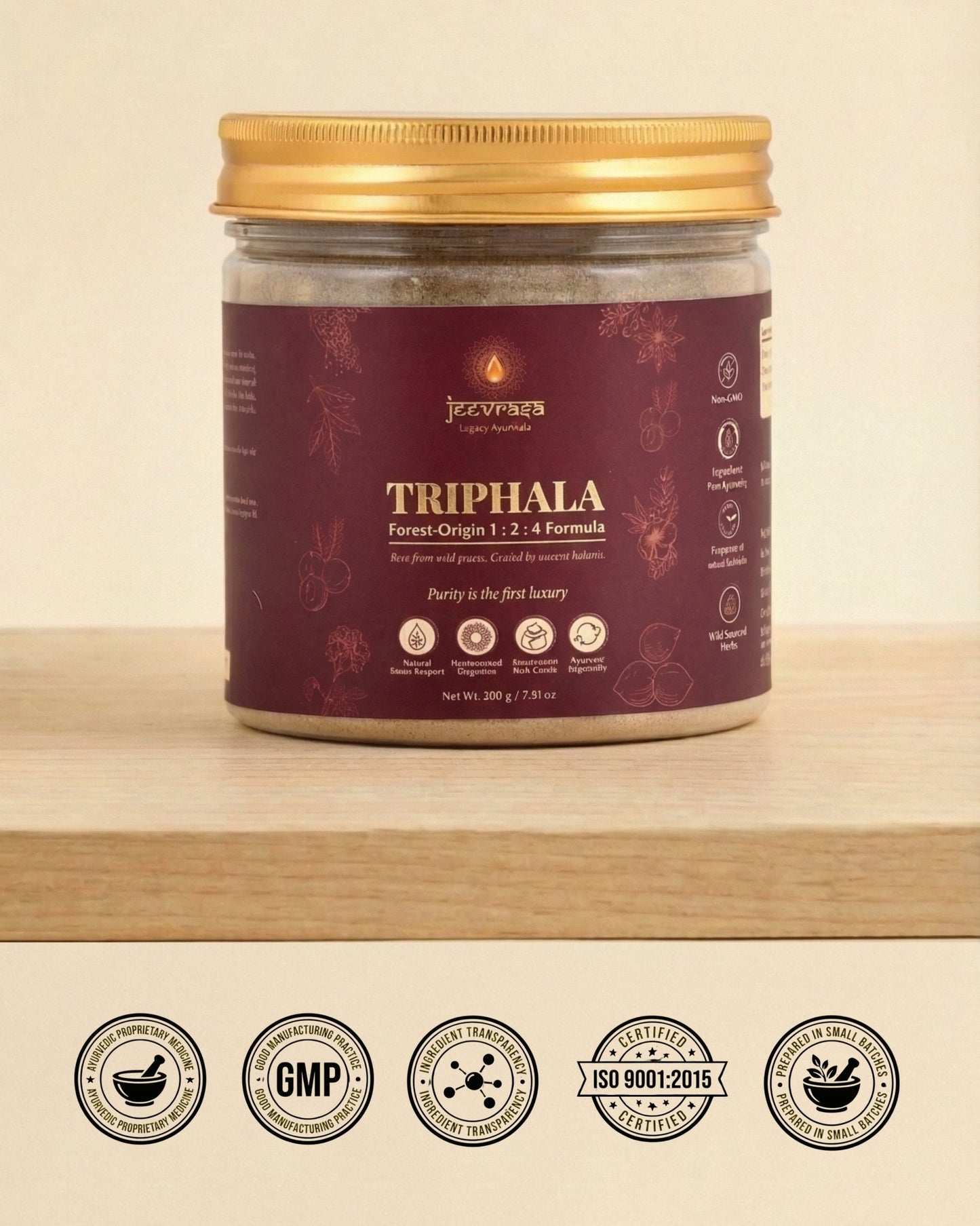 Jar of Triphala powder with a gold lid on a wooden surface, featuring certification logos at the bottom.