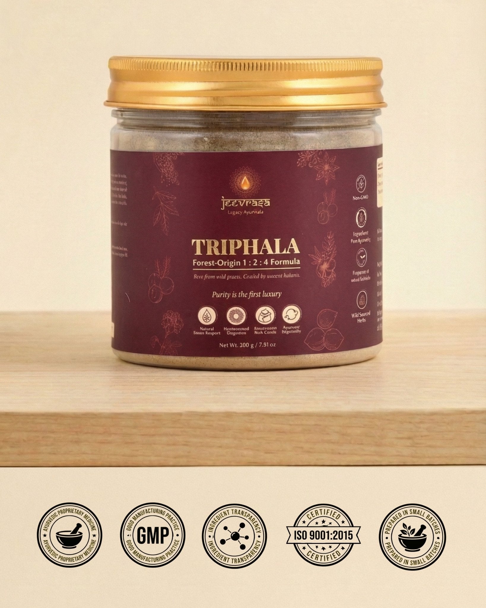 Jar of Triphala powder with a gold lid on a wooden surface, featuring certification logos at the bottom.